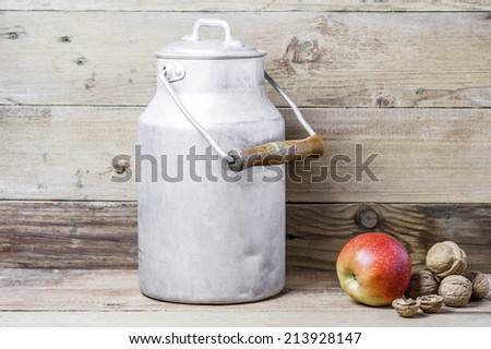 An apple, walnuts and an aluminum old milk can on a wooden background