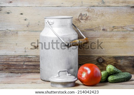Red tomato, green cucumbers and an aluminum old milk can on a wooden background