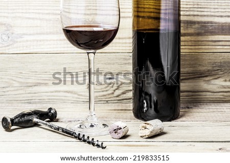 Wine glass, broken cork, corkscrew and bottle on a wooden background