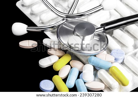 Close-up of phonendoscope, medicine color tablets and white capsules in the blister on a black background