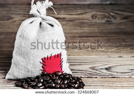 Concept of the thrift storing.  Coffee beans in the burlap sack with the patch on a wooden background