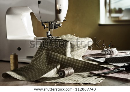 Sewing machine, fabric, scissors, spools of thread on window background