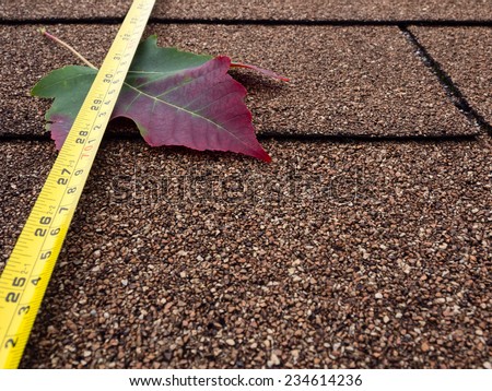 Tape measure and autumn leaf on asphalt shingles