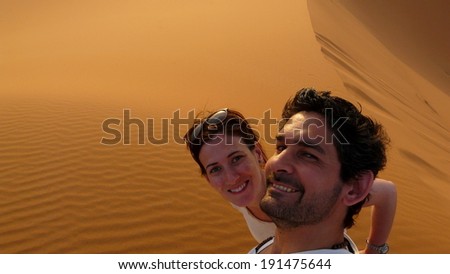 A young couple taking a self picture while climbing to the top of the Great Sand Dune in the red dune sea of Erg Chebbi, Morocco.