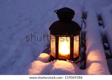 Candle lamp on snowy bench at dusk