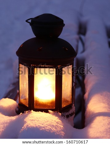 Candle lamp on snowy bench at dusk