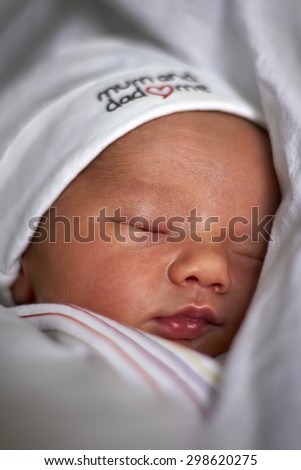 Portrait of a sleeping peaceful newborn boy with a white hat wrapped in a white blanket