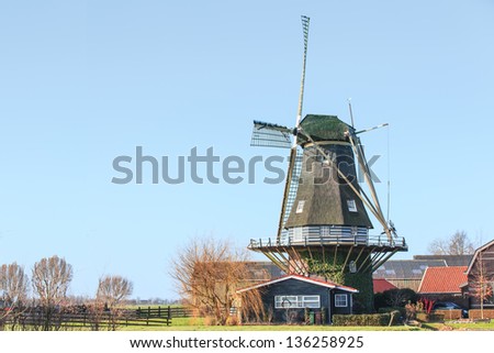 Flour mill with millers cottage on a dike in the Netherlands overlooks a smock on a blue cloudless sky