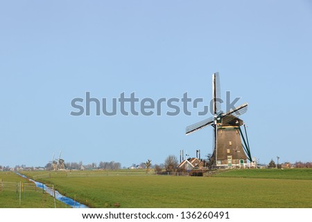 Dutch polder landscape with a windmill against a bright blue sky and two windmills at te background