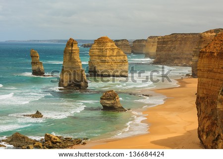 Blue green ocean and beach with sandbanks cliffs and waves  with close view of The twelve apostles and cliffs in the shadow of the late afternoon sun in Victoria, Australia against a blue cloudy sky