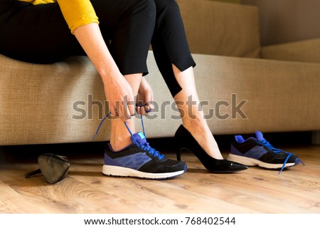 Woman changing high heels, office shoes after working day while sitting on the couch, ready to take a walk or run