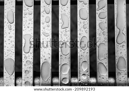 Raindrops creating patterns on metal bars on a seat