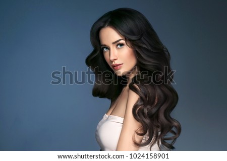 Woman perfect hair beautiful female portrait over blue background. Brunette haircare long curly hairstyle beauty concept