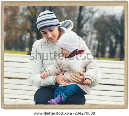 Family mother with child walking in park in autumn season in same white clothes and stripes cap on rainy day. Mother hold the hand baby, road in the autumn park