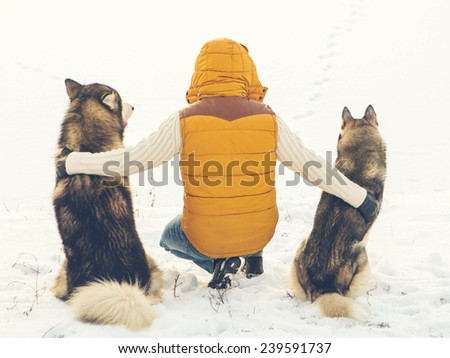 Man with dog Huskies back sit on snow. Friendship animal dog and man