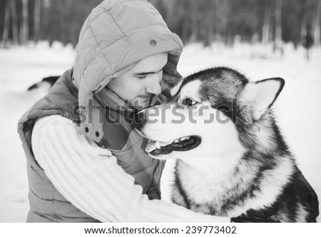 Man walking with dog winter time with snow in forest Malamute and Huskies friendship black and white