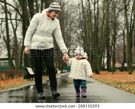 Family mother with child walking in park in autumn season in same white clothes and stripes cap on rainy day. Mother hold the hand baby, road in the autumn park