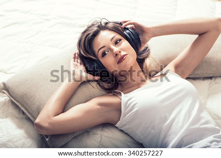 Young beautiful woman headphones listening music on bed top view