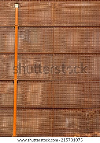 Rusted metal construction with a rusty long alone pipe.  Perforated, punched, hole metal panels.