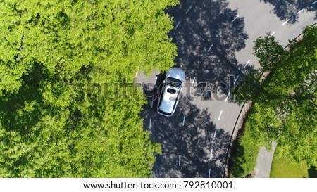 Aerial top-down photo silver grey self driving test car driving through corner simple two lane road with trees left and right at side of road