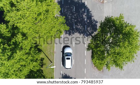 Aerial top-down photo silver grey self driving test car driving over straight road simple two lane road with trees left and right at side of road