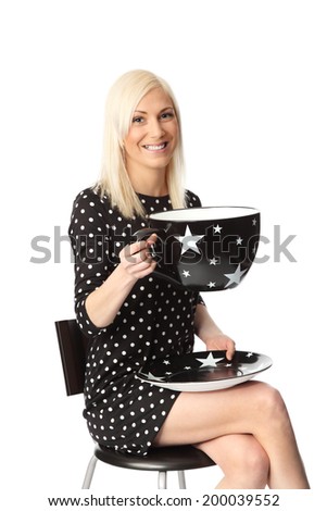 Cute woman with a black spotted dress holding an oversized coffee cup. White background.