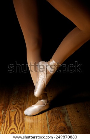Closeup of a ballerina\'s feet in pointe shoes on a vintage, wood floor with black background.