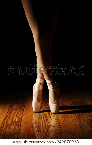 Closeup of a ballerina\'s feet in pointe shoes on a vintage, wood floor with black background.