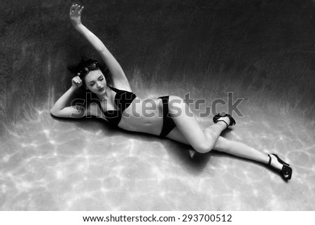 Sassy image of a woman swimming underwater in a bikini and sunglasses