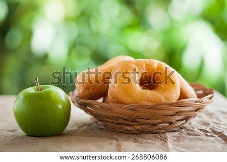 Cake donuts and green apple on the table outside the house. natural light with blurred background effect of trees in the garden