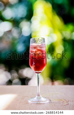 glass with ice cubes and grape flavored beverage background blurring of trees in a park. The purpose of this blur effect to indicate freshness, organic and natural environment.