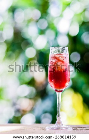 glass with ice cubes and grape flavored beverage background blurring of trees in a park. The purpose of this blur effect to indicate freshness, organic and natural environment.