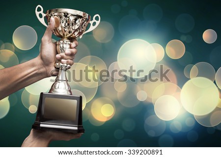 hand holding up a gold trophy cup as a winner in a competition