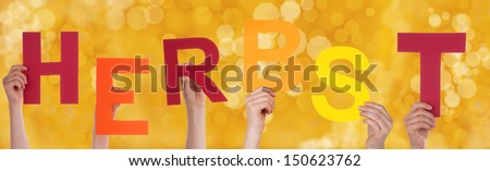 Many Hands Holding the German Word Herbst Which Means Fall or Autumn with a Yellow Background