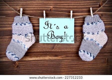 A Light Blue Label With The Words It Is A Boy On It Hanging On A Line With Baby Socks