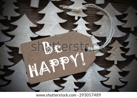 Brown Christmas Label With Ribbon On Wooden Christmas Trees Background. Vintage Style. Label With English Text Be Happy For Christmas Or Season Greetings.Close Up Or Macro