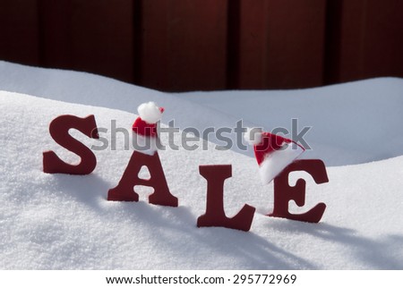Red Wooden Letters With Santa Hat Building Word Sale In Christmas Time Or Season Snow And Snowy Scenery In Front Of Red Wooden Background. Christmas Atmosphere