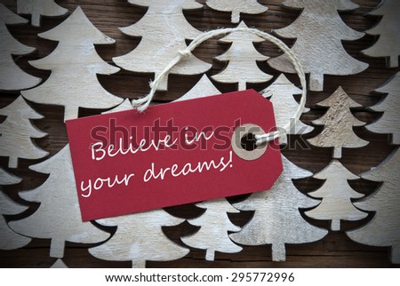 Red Christmas Label With Ribbon On Wooden Christmas Trees Background. Vintage Or Rustic Style. Label With English Text Believe In Your Dreams For Christmas Or Season Greetings.Close Up Or Macro