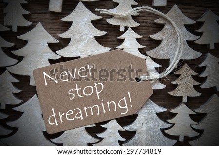 Brown Christmas Label With Ribbon On Wooden Christmas Trees Background. Vintage Style. Label With English Quote Never Stop Dreaming For Christmas Or Season Greetings.Close Up Or Macro