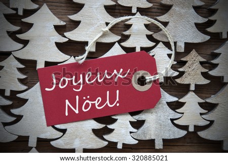 Red Christmas Label With Ribbon On Wooden Christmas Trees Background. Vintage Style. Label With French Text Joyeux Noel Means Merry Christmas For Christmas Or Season Greetings.Close Up Or Macro
