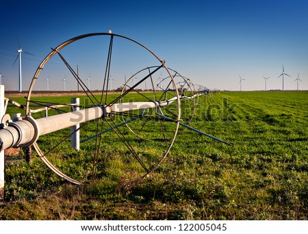 Water irrigation in a rural field with wind turbines in the background