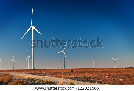 Several large wind turbines in a wind farm located in West Texas.  A dirt Road is in the foreground