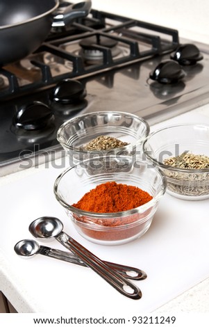 Herbs and spices used in cooking preparation.  Gas range with wok shown in background.  Focus is on nearest spice bowl.