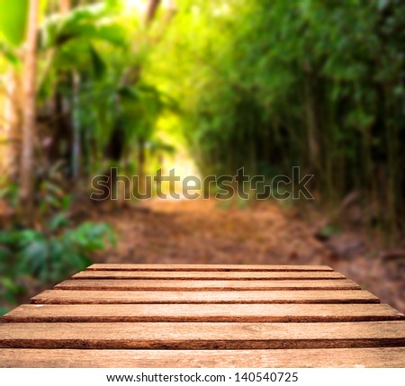 Old weather worn plank table top with tropical jungle path in background.  Focus is on planks in foreground