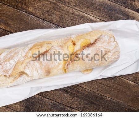 Fresh baked rustic bread loaves on paper bag on dark wood background