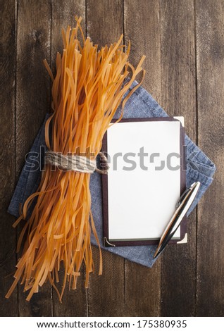 Bunch of raw tagliatelle pasta with notebook paper on wooden table