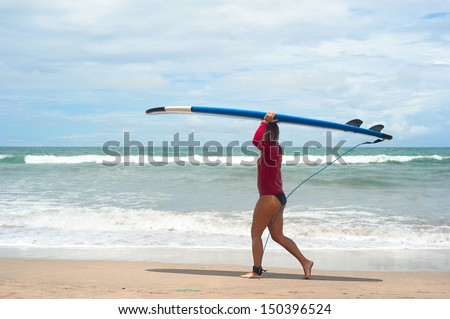 BALI, INDONESIA - MARCH 09: Unidentified woman walking with a surfboards on the beach on March 09, 2013 in Bali island; Indonesia. Bali is one of the top of world surfing destinations.