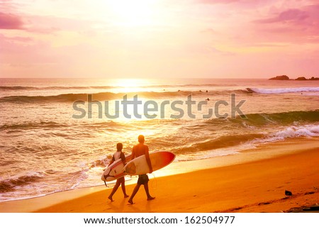 Couple of surfers walks along the beach in Hikkaduva - is the best surf paradise in Sri Lanka