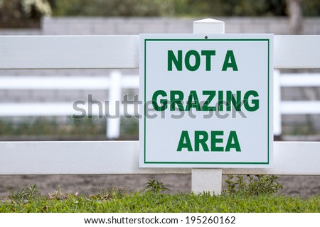 White not a grazing area sign mounted on a wooden fence with green letters outside of an equestrian arena.