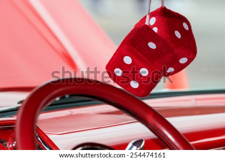 Two fuzzy dice hanging from the rear view mirror on a classic car.